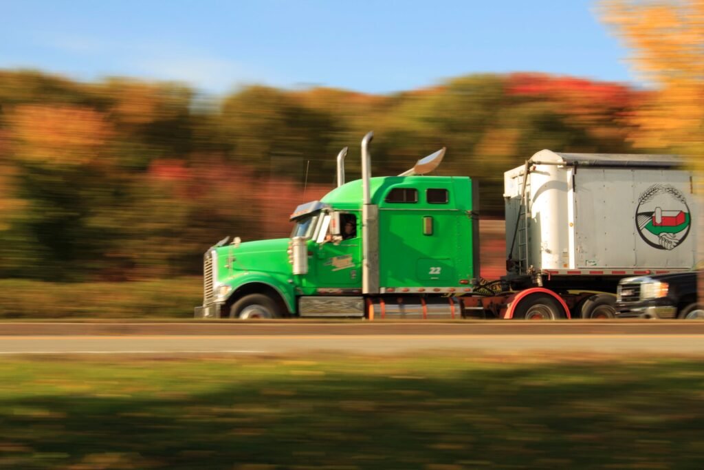 Green truck driving with trees in the background